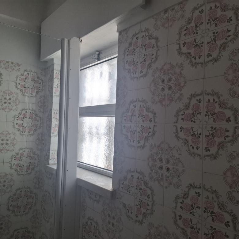 Bathroom with decorative pink floral tiles, glass shower door, and a frosted window letting light in