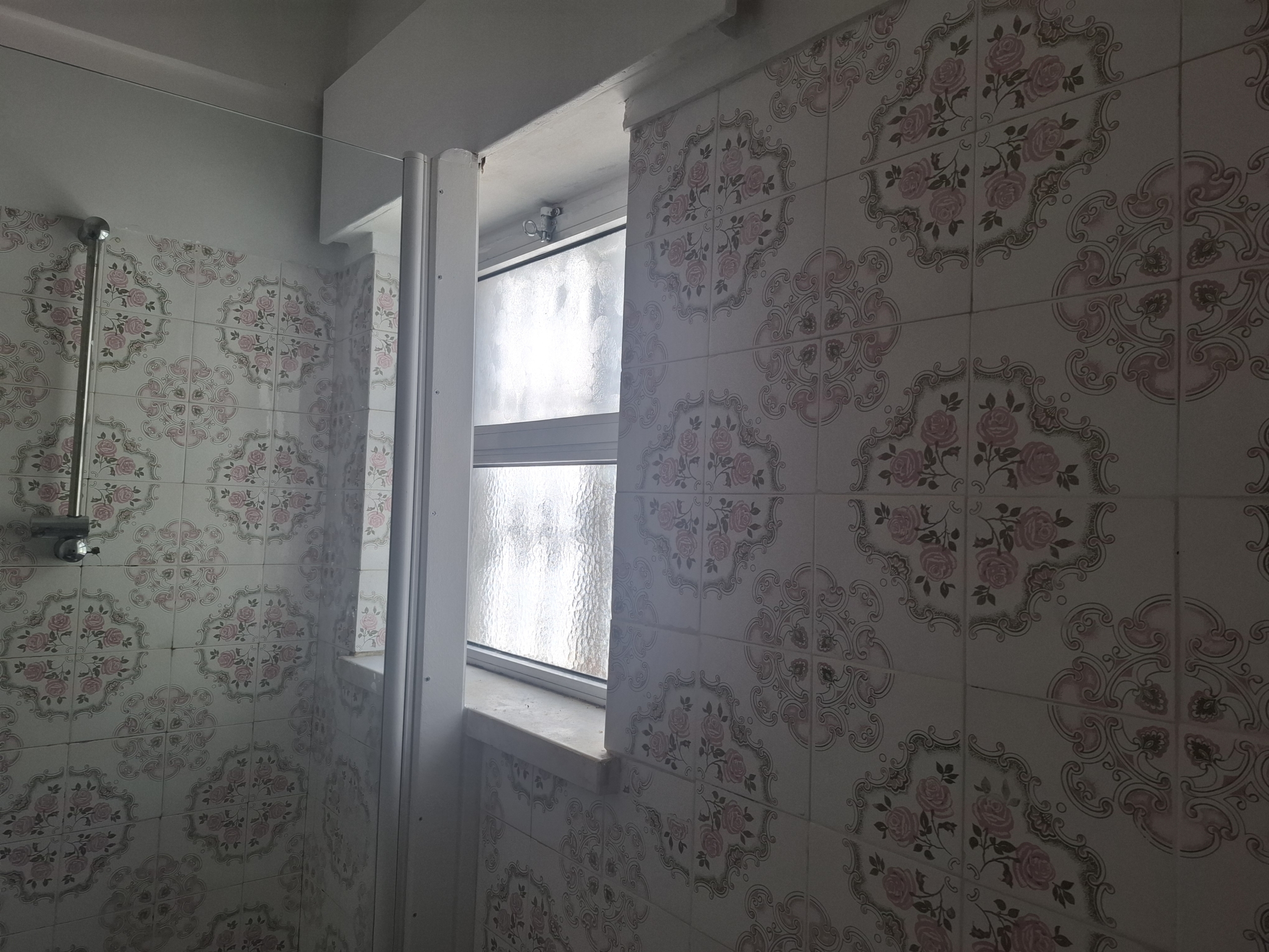 Bathroom with decorative pink floral tiles, glass shower door, and a frosted window letting light in