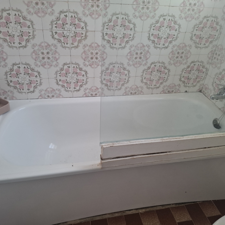 White bathtub against a wall covered in pink floral patterned tiles; chrome faucet visible on the right and a pink soap dish on the edge.