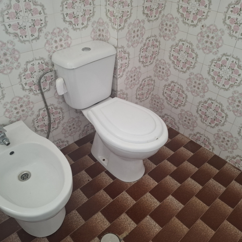 White toilet beside a bidet in a bathroom with pink floral patterned wall tiles and brown tiled floor