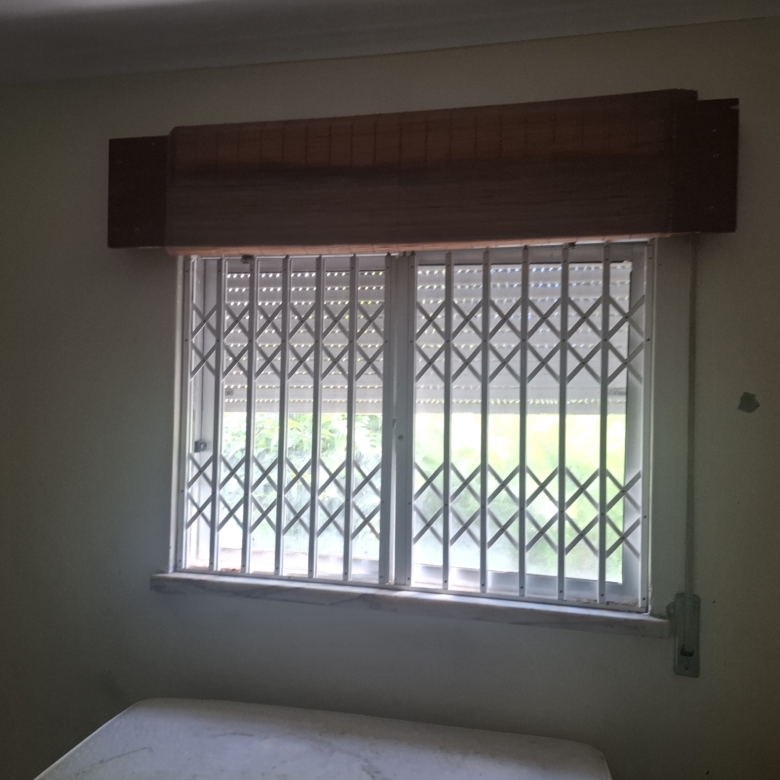 Bedroom window with white metal security bars and a dark wooden valance above the sill.