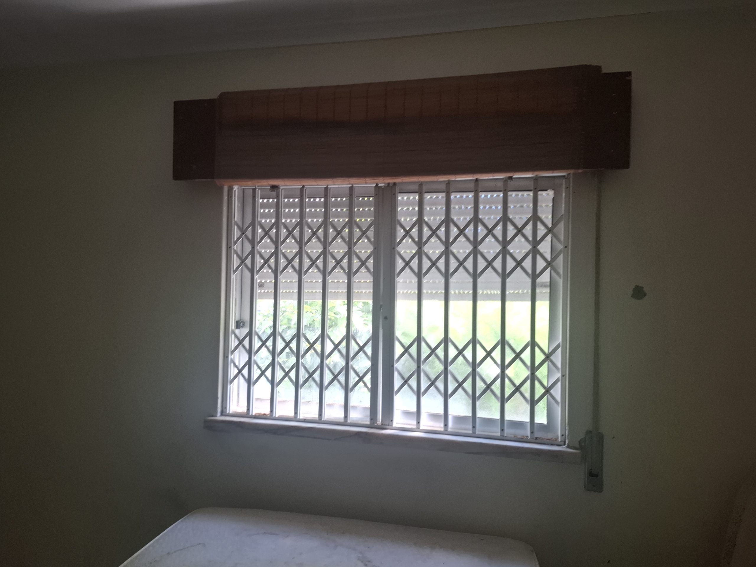 Bedroom window with white metal security bars and a dark wooden valance above the sill.