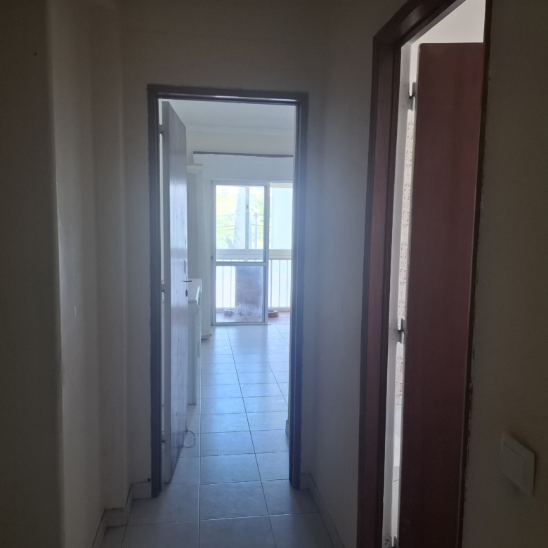 Narrow hallway with open doorways opening to a bright room with large windows and a balcony outside the doors.