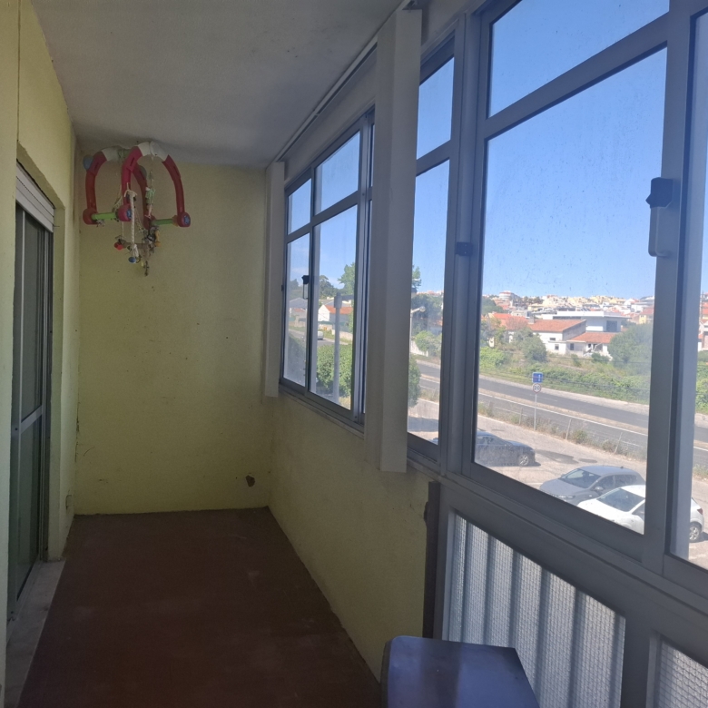 Narrow corridor balcony with large windows on the right, yellow walls, and a colorful hanging toy or mobile near the far wall on the left side.