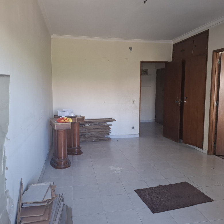 Empty room under renovation with piles of wooden planks, a small pedestal table, beige walls, and open brown cabinet doors.