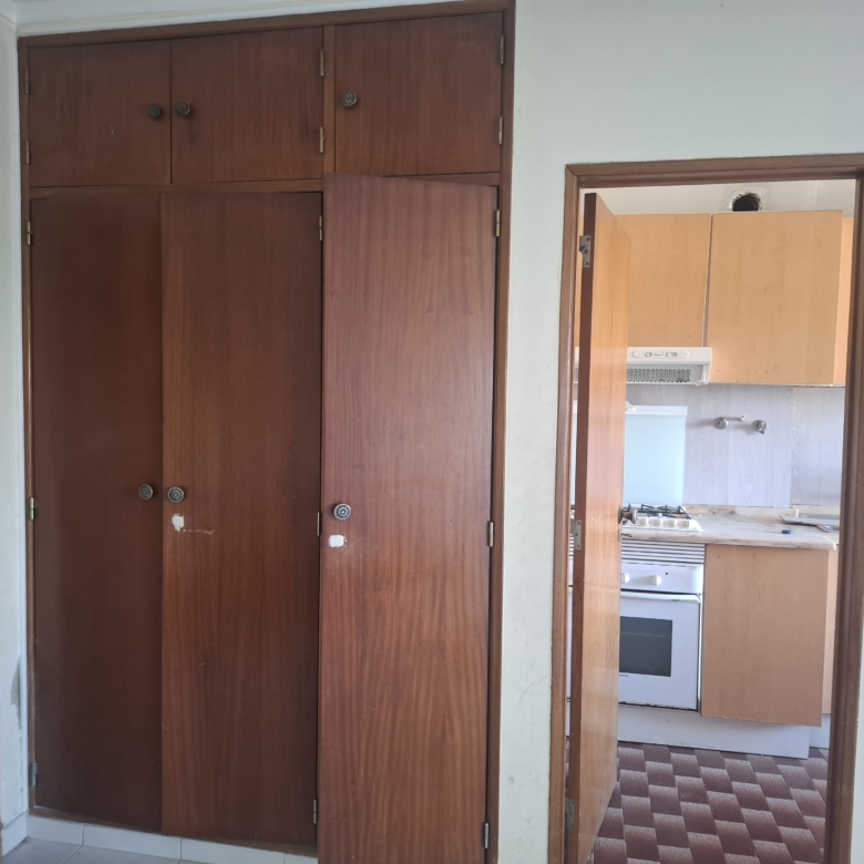 Interior view of a doorway leading to a kitchen; tall wooden wardrobes cover the left wall, with a visible stove oven through an open door on the right.