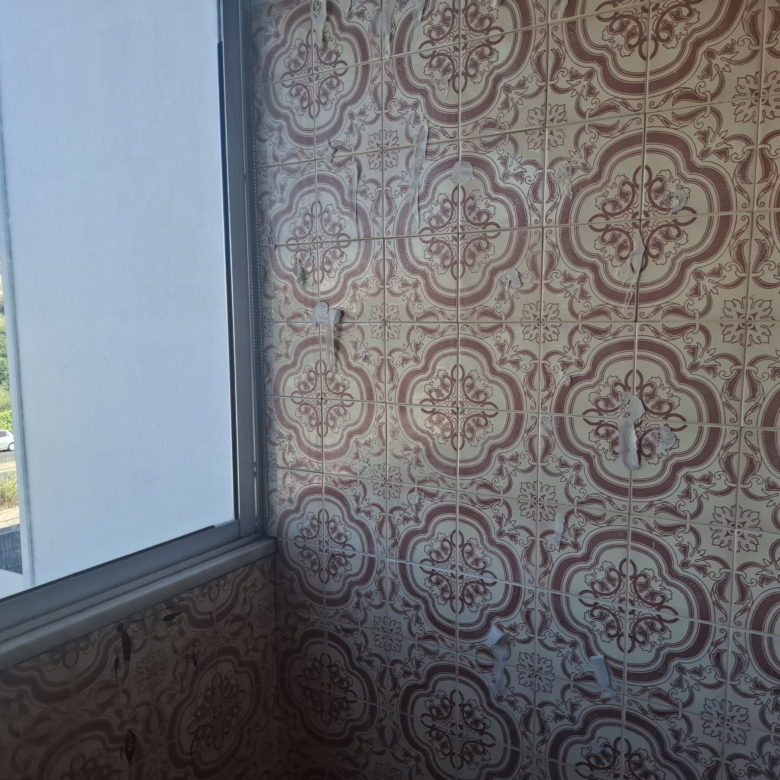 Interior corner with brown ornate patterned tiled wall; window on the left shows blue sky and a distant construction site.