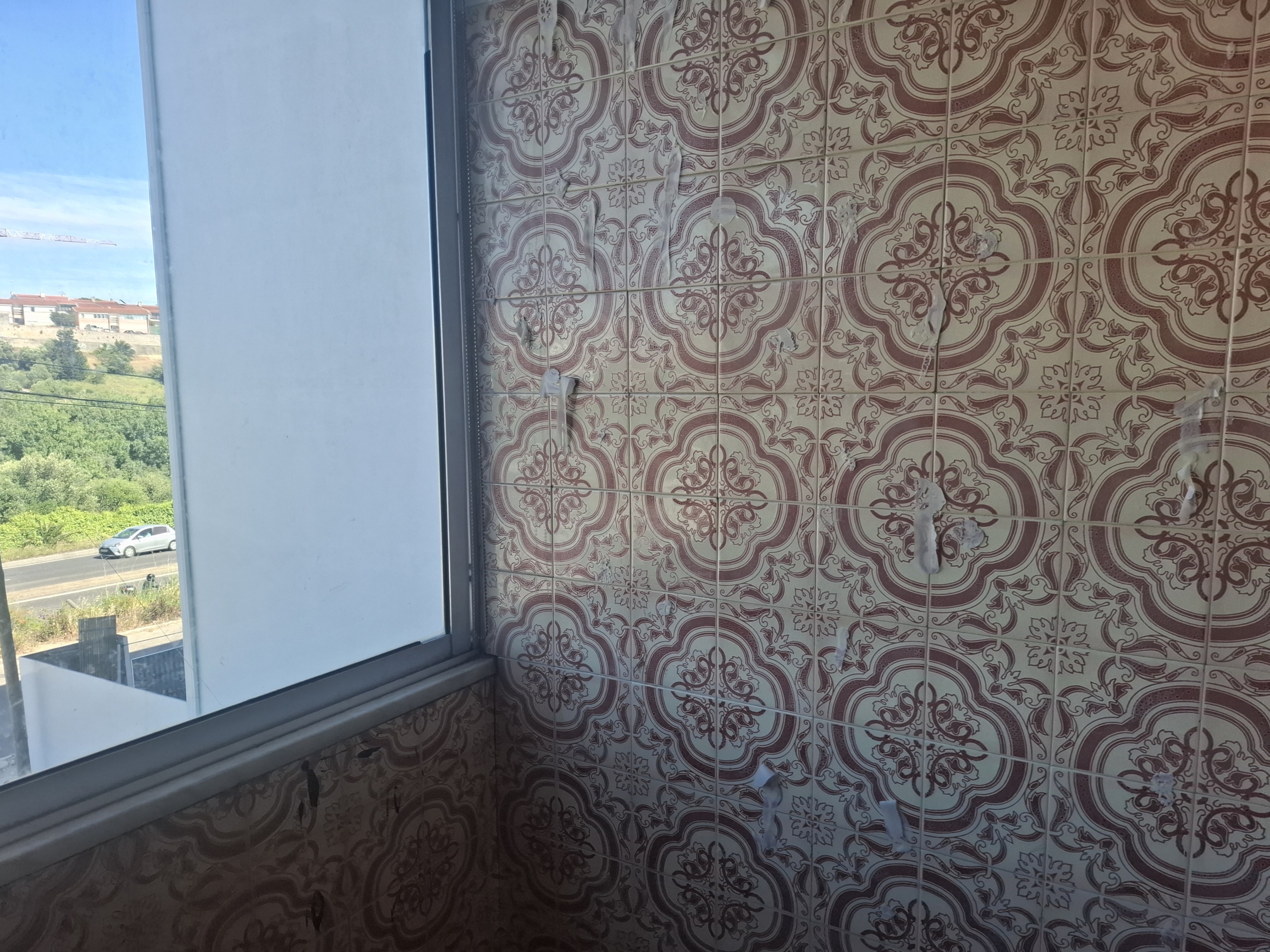 Interior corner with brown ornate patterned tiled wall; window on the left shows blue sky and a distant construction site.