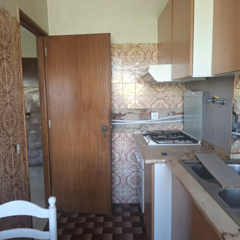 Old kitchen with pink patterned wall tiles, a wooden door ajar, a gas stove, and a double sink visible to the right.