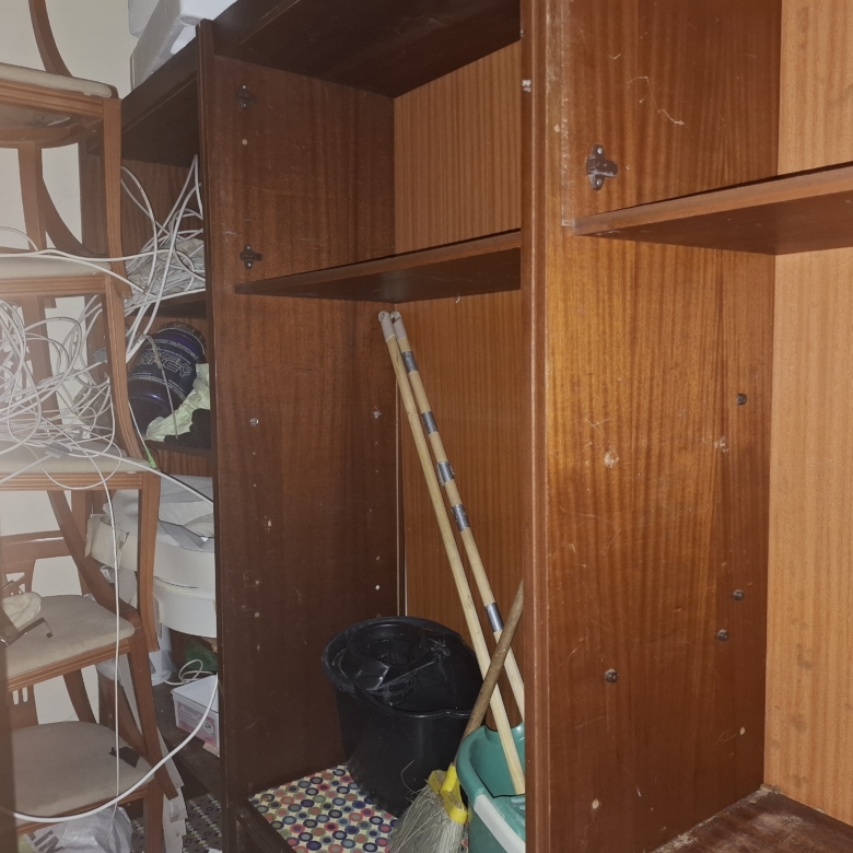 Messy storage cabinet interior with tangled cables, wooden shelves, and scattered household items like a mop and bucket.