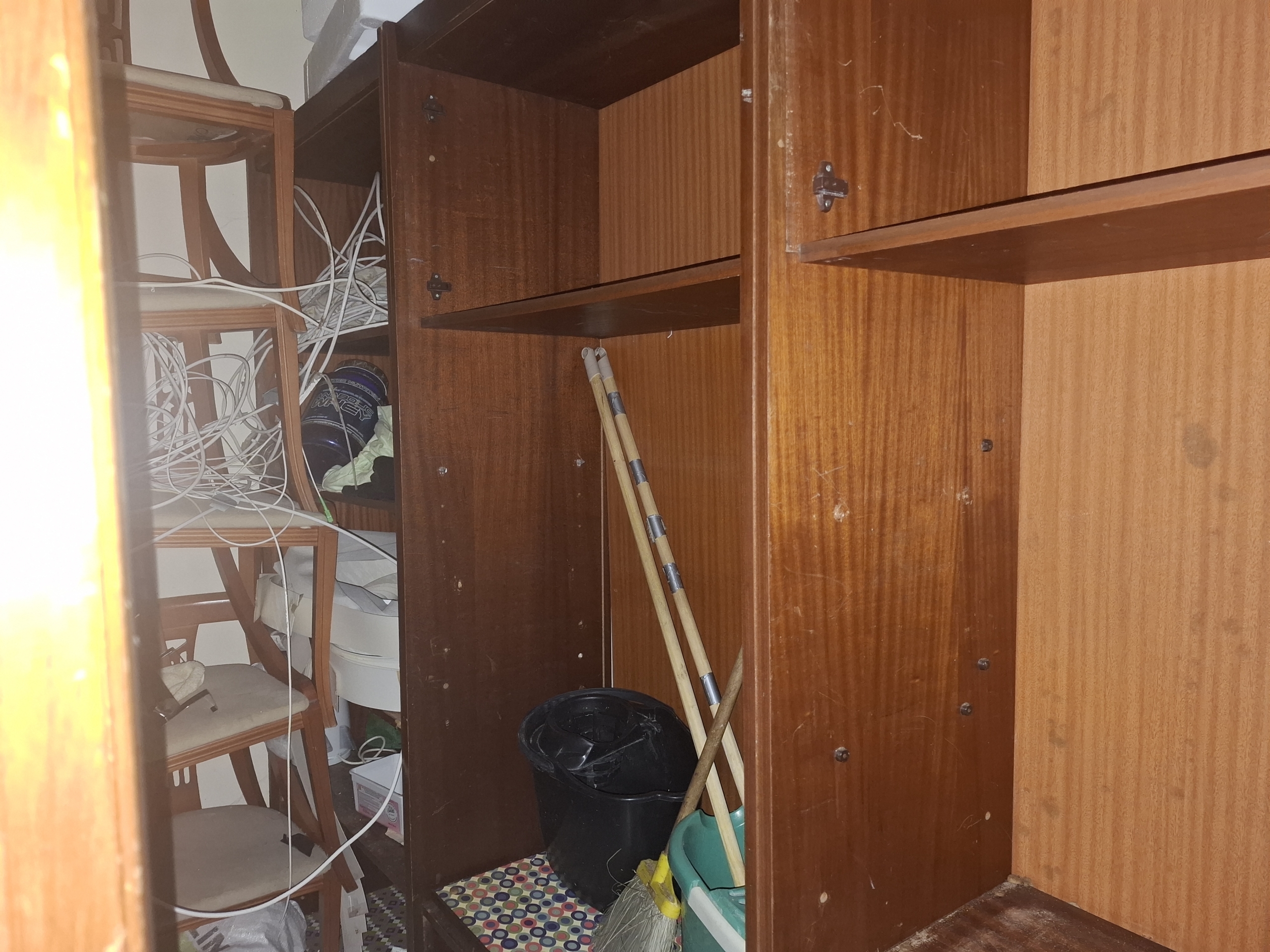 Messy storage cabinet interior with tangled cables, wooden shelves, and scattered household items like a mop and bucket.