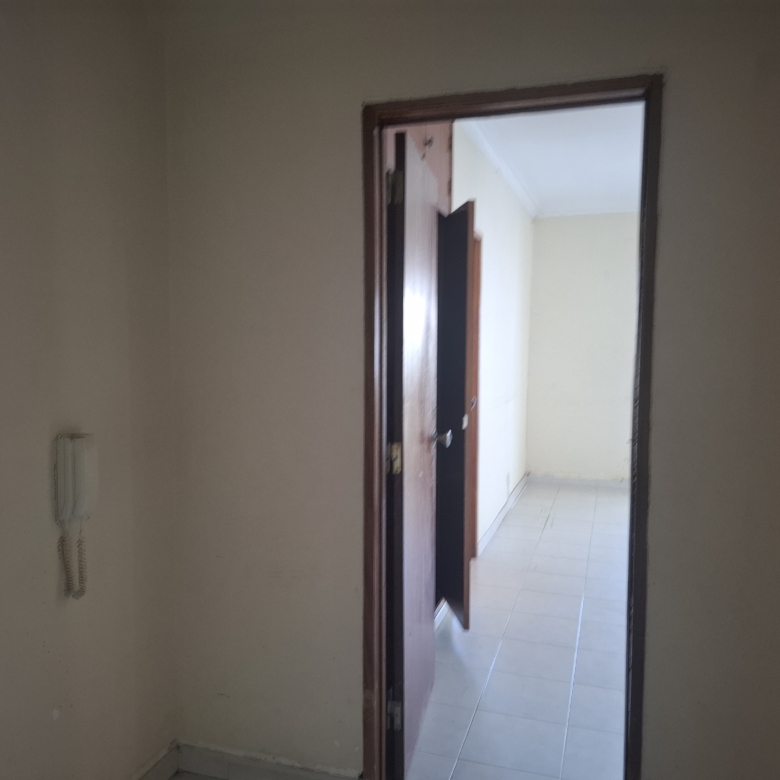 Interior doorway: open wooden door appears to lead from a beige-walled room into a light-colored tiled space beyond.