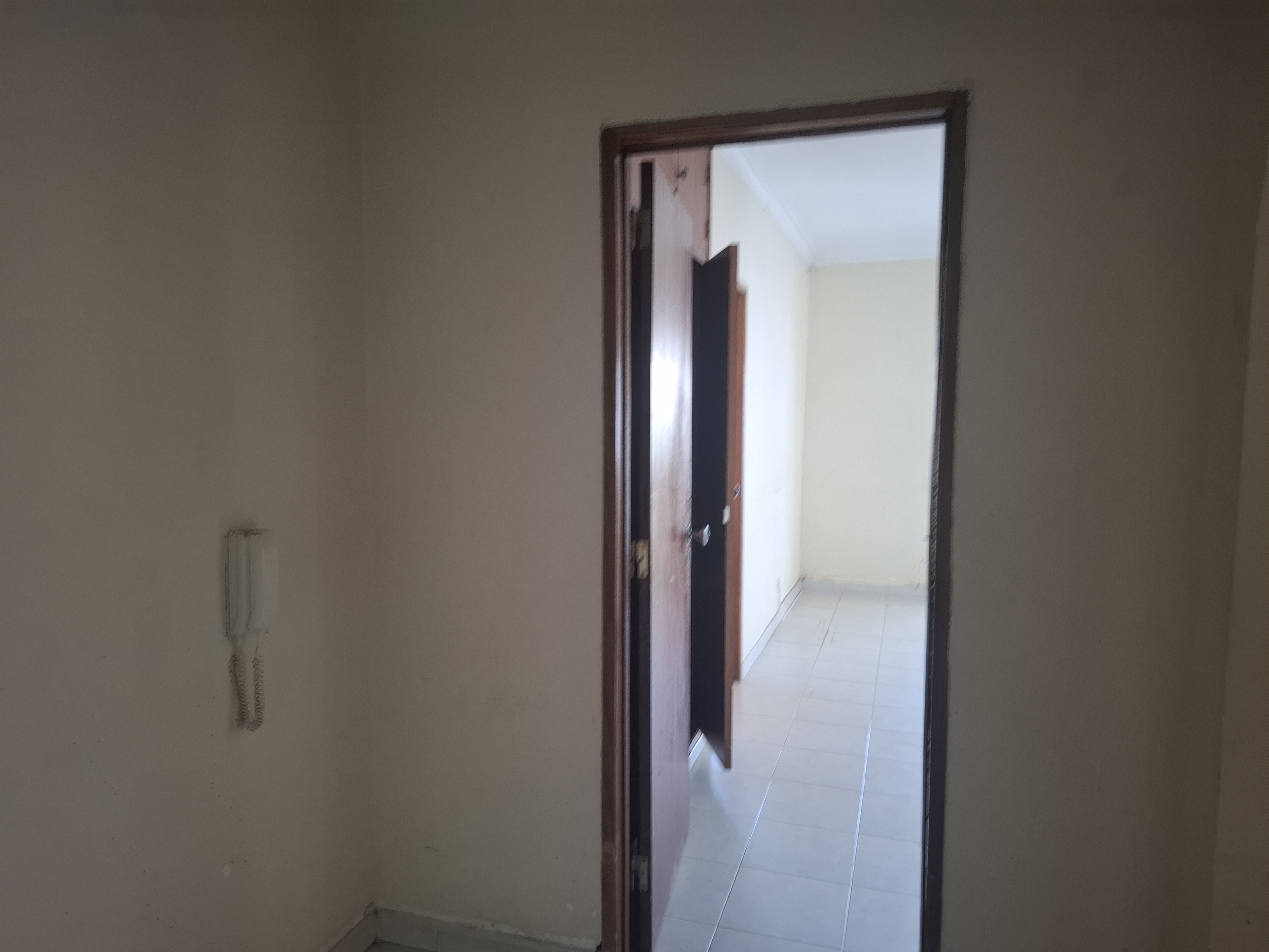 Interior doorway: open wooden door appears to lead from a beige-walled room into a light-colored tiled space beyond.