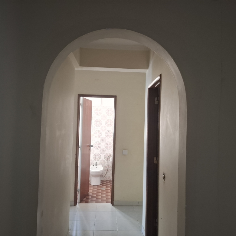 Narrow hallway with an arched doorway opening into a bathroom; toilet visible beyond the doorway.