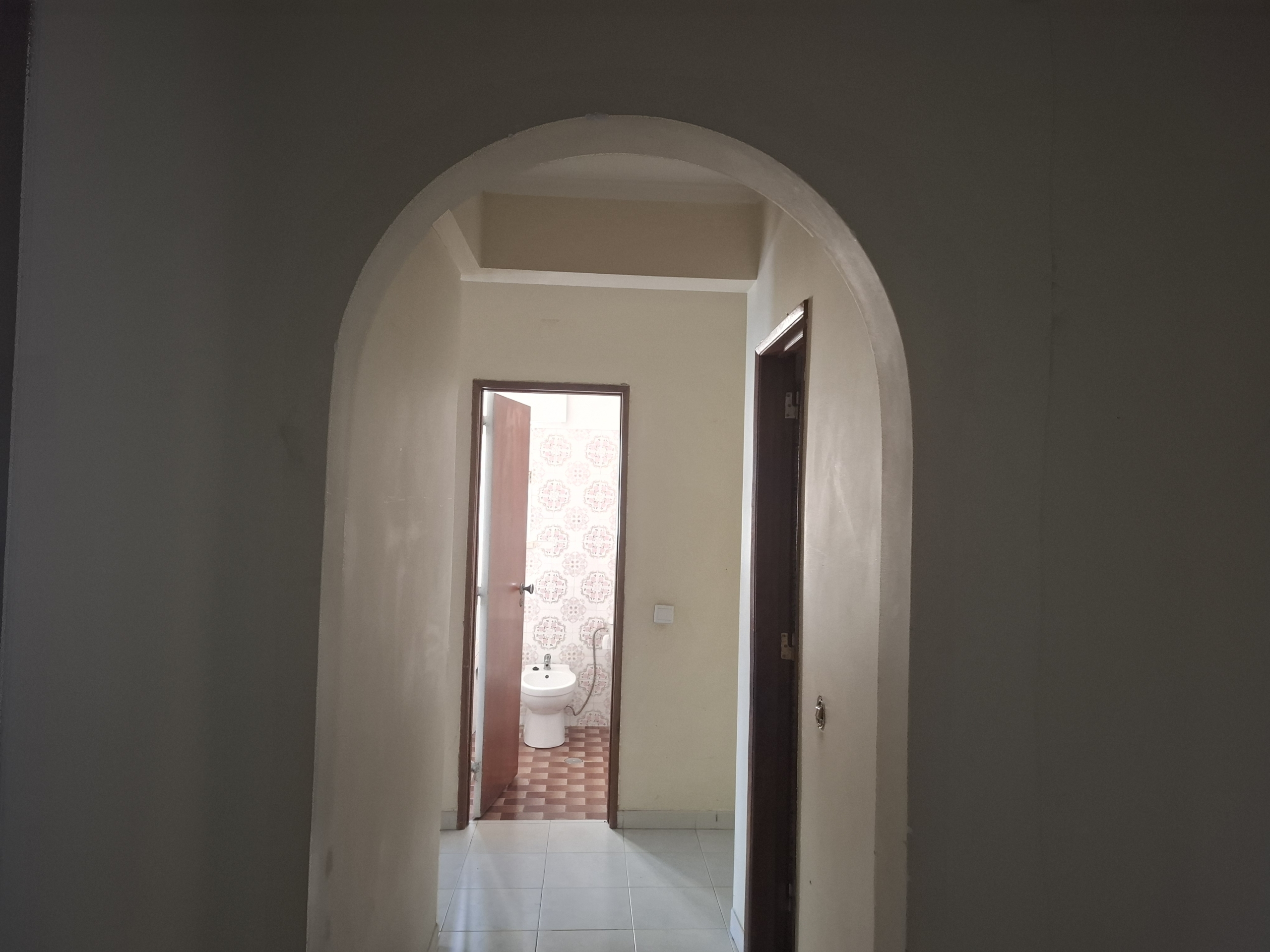 Narrow hallway with an arched doorway opening into a bathroom; toilet visible beyond the doorway.