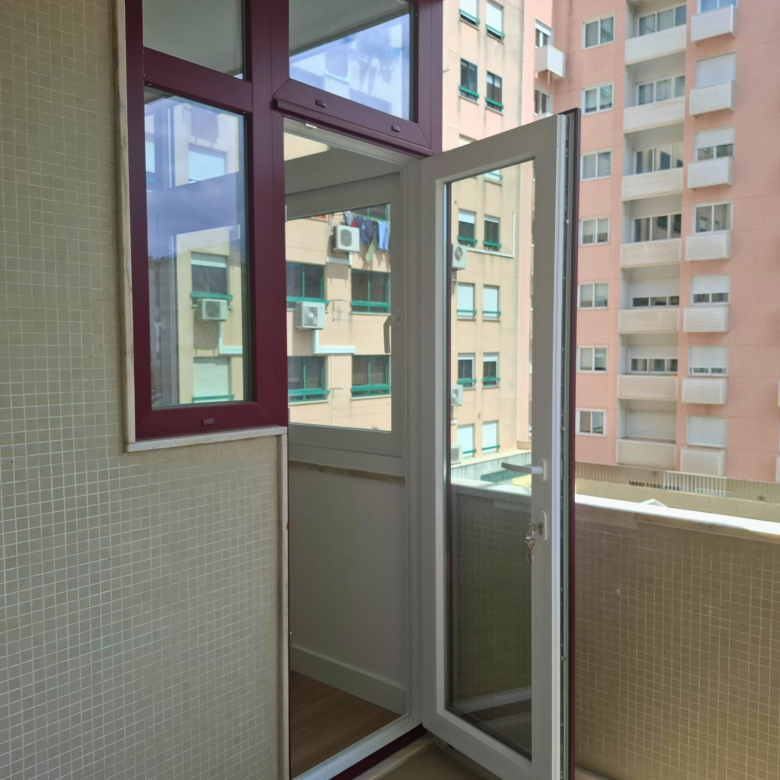 Open glass door to a tiled balcony, showing an urban building with windows and visible air conditioning units outside.