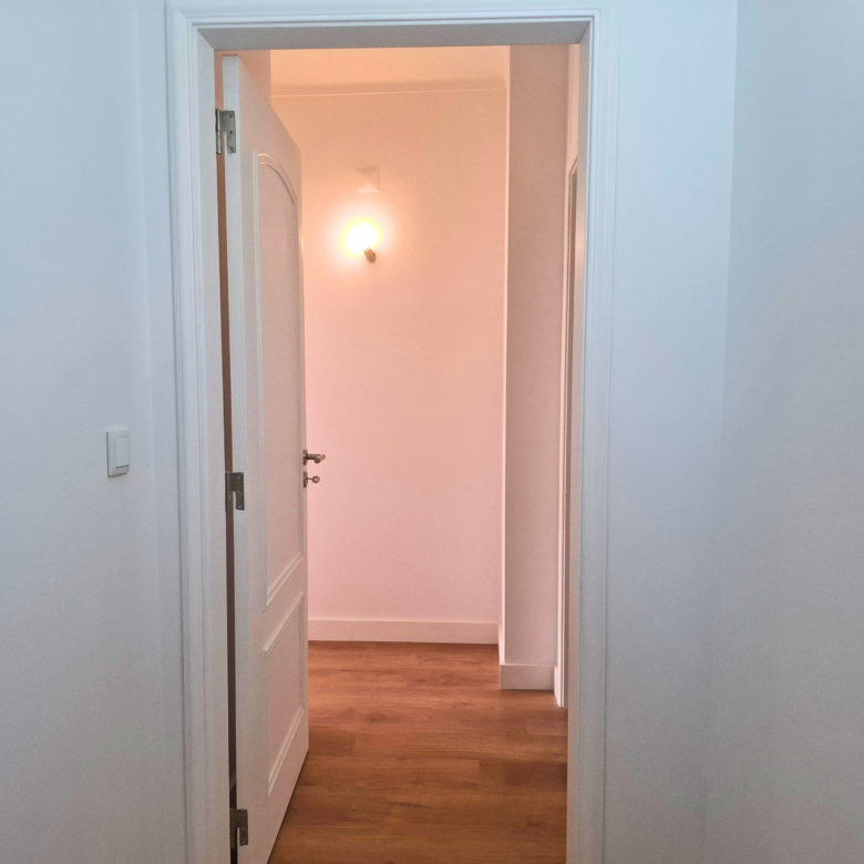 White doorway opening into a softly lit hallway with a warm wall sconce glow at the end of the corridor.