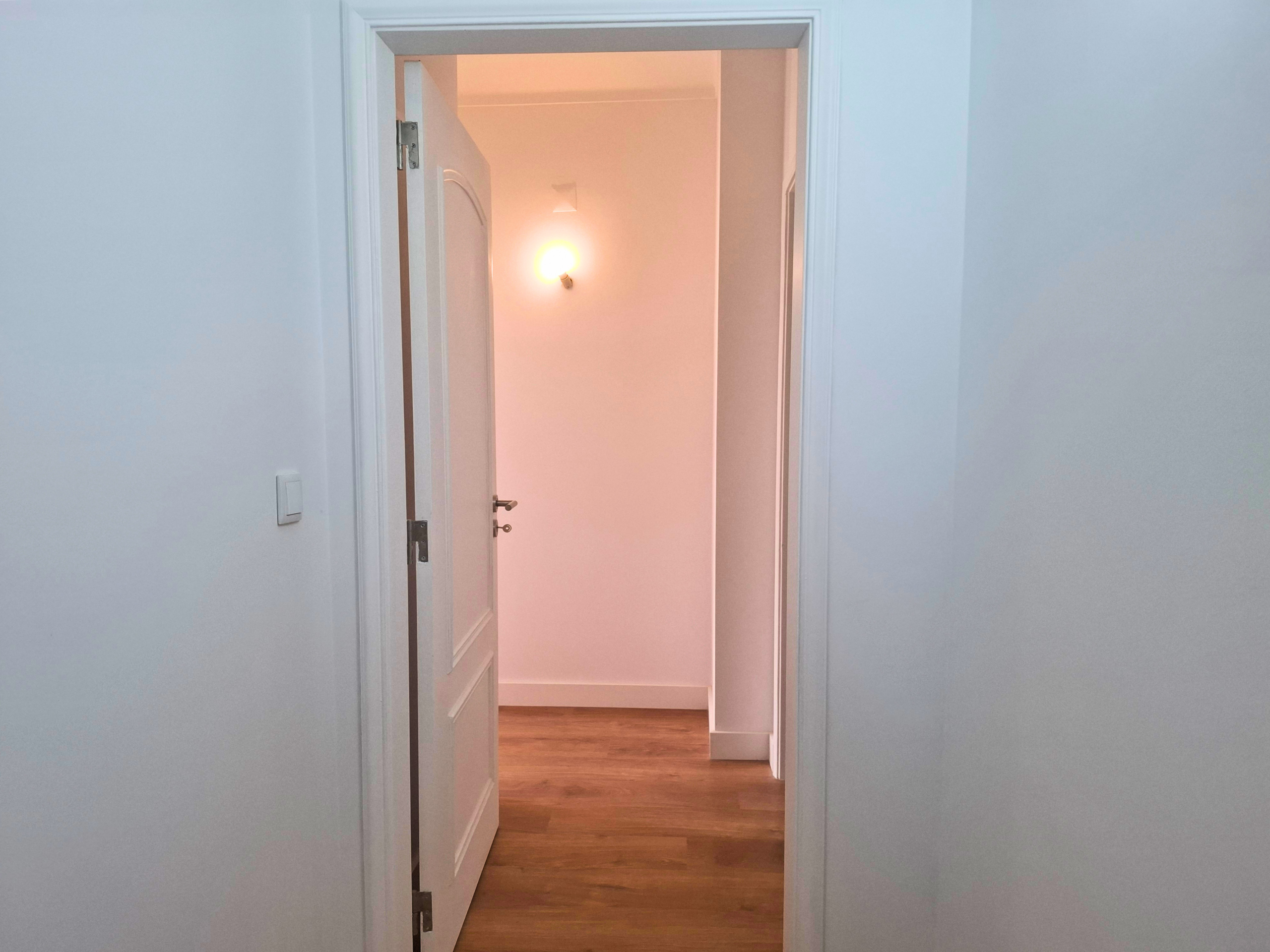White doorway opening into a softly lit hallway with a warm wall sconce glow at the end of the corridor.